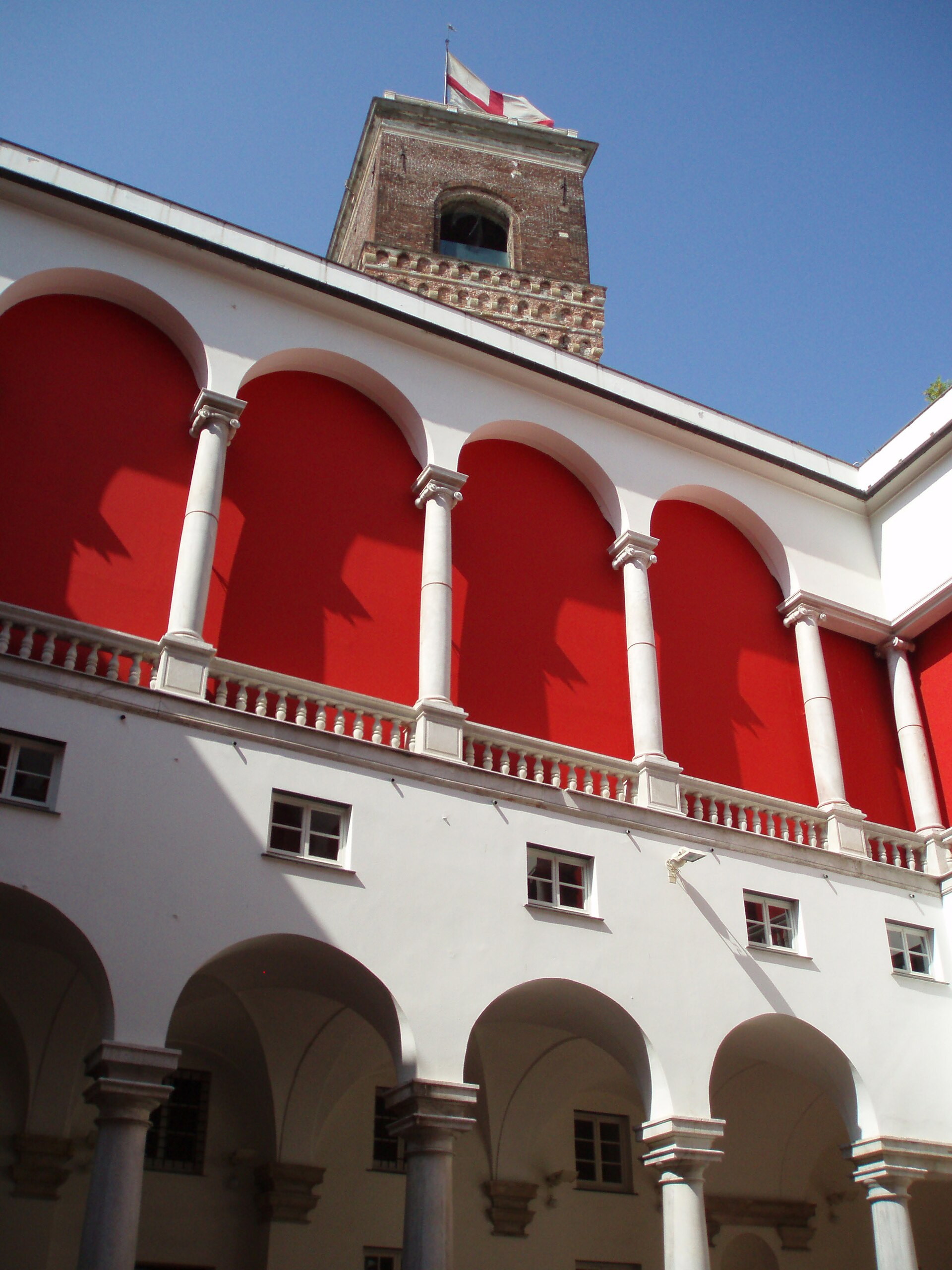 Facciata di cortile con archi sovrapposti e torre, palazzo pubblico italiano.